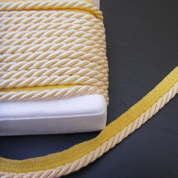 Twisted flanged piping cord 7mm wide in custard color from the reel on black background
