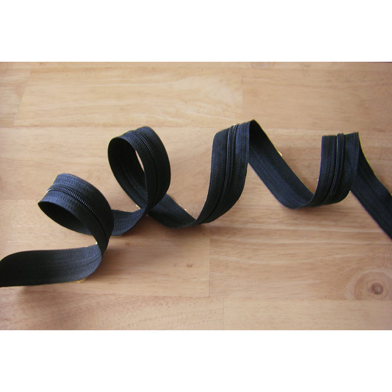 Plastic, nylon, Continuous zip - black, size 3, twisted on wooden table Plastic, nylon, Continuous zip - black, size 3, twisted on wooden table