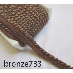 Twisted flanged piping cord 7mm wide in bronze color from the reel on white background