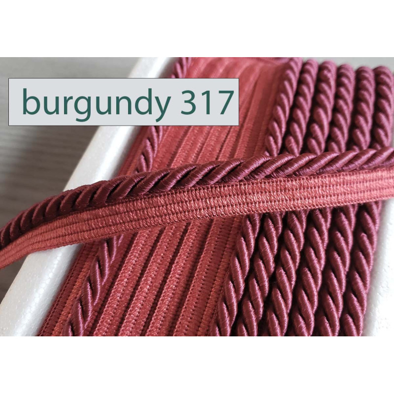 Twisted flanged piping cord 7mm wide in burgundy from the reel on a white table