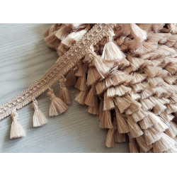 Tassels trim in beige sand color on the reel, 50mm long placed on the table