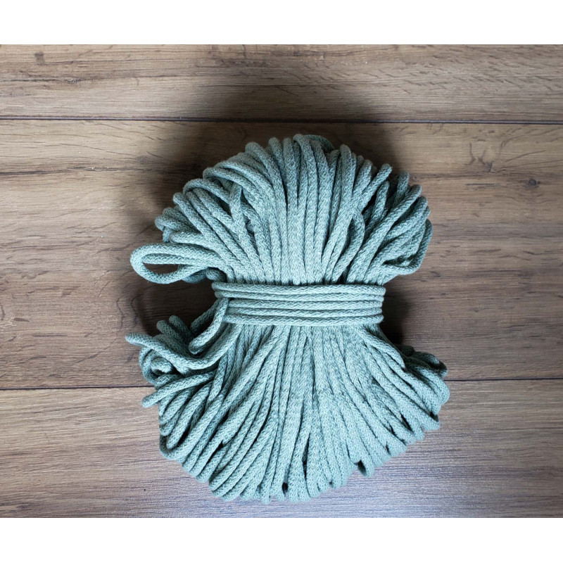 Cotton braided cord in sage green color, the full reel of cord on a wooden table