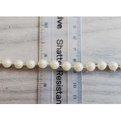 round pearl trim - ivory  twisted on a grey background with a ruler