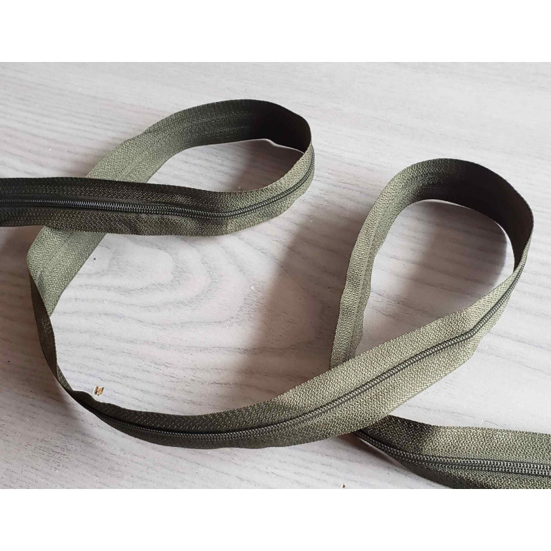 Plastic, nylon, Continuous zip - Olive size 3, twisted on wooden table Plastic, nylon, Continuous zip - Olive size 3, twisted on wooden table