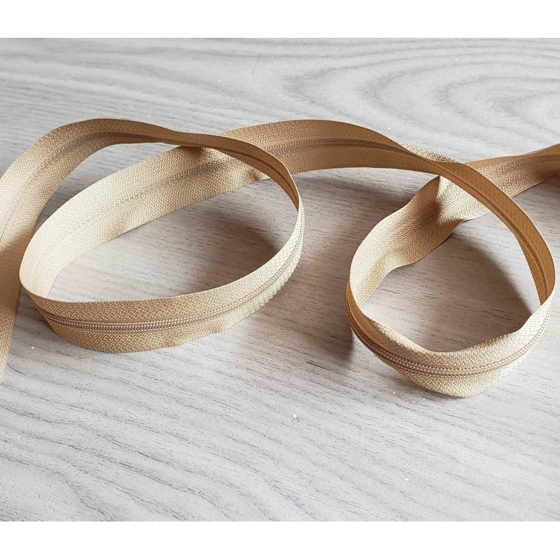 Plastic, nylon, Continuous zip - Light beige size 3, twisted on wooden table Plastic, nylon, Continuous zip - Light beige size 3, twisted on wooden table